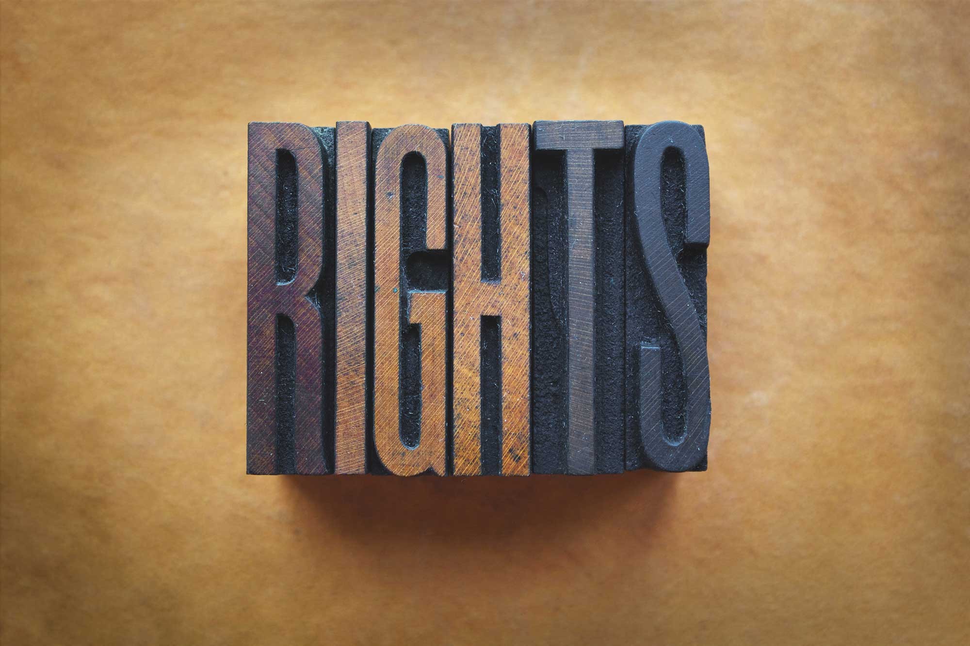 the word “rights” carved out of wood painted in hues of brown tan and blue