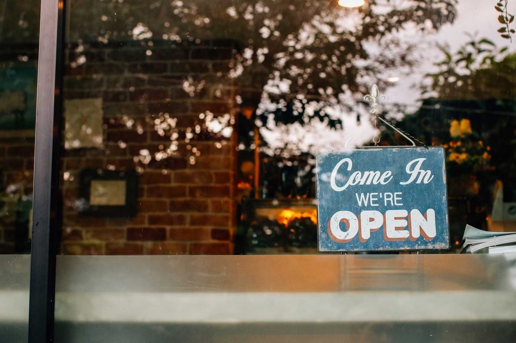 looking in a large storefront window with reflections in the glass and a sign that says “Come in, We’re Open"