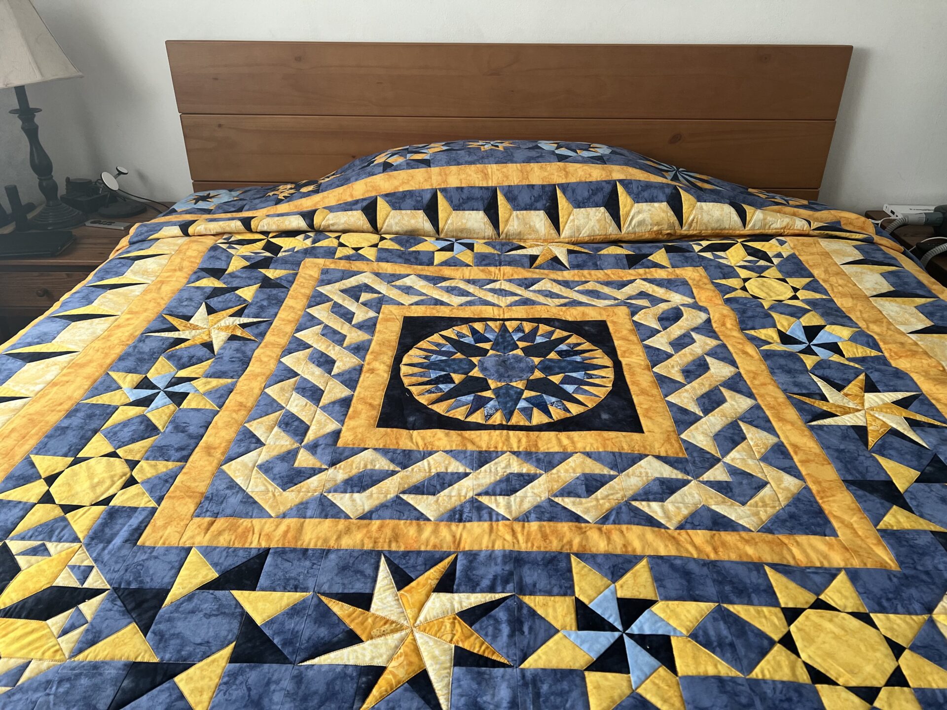A blue, yellow, and gold tumbling blocks quilt on a king sized bed.