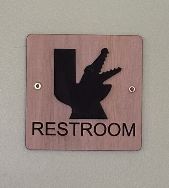 Restroom sign with the silhouette of a commode with a gator coming out.