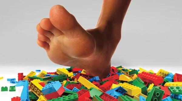A LARGE SHOELESS FOOT STEPPING ON A PILE OF LEGOS 