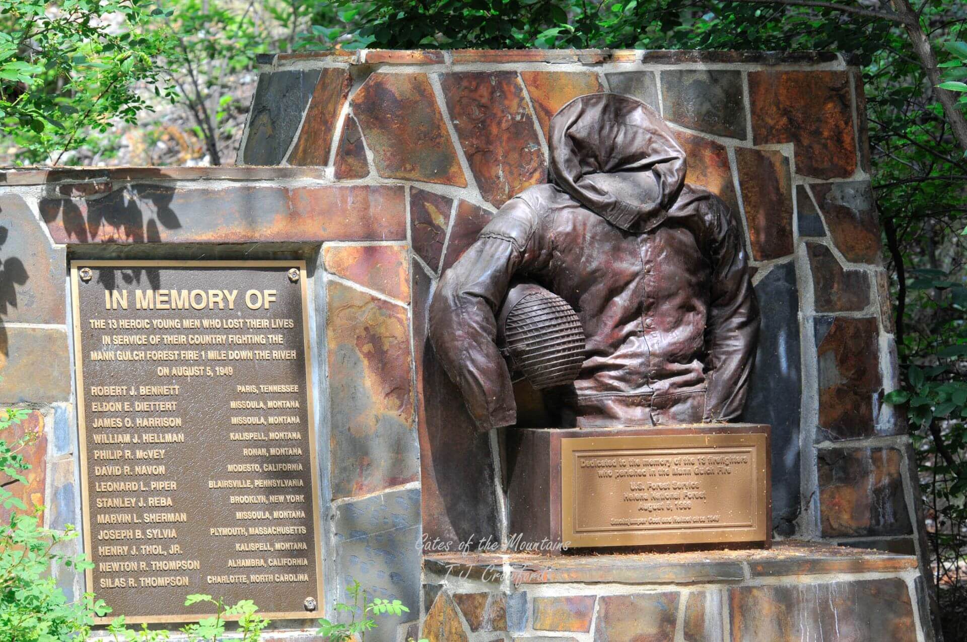 Image of the monument to the 13 smokejumpers killed in the Mann Gulch fire. On the left is the list of their names and their hometowns. On the right is a a statue of the suiot of a smokejumper's torso. It is empty to signify the loss of the 13 smokejumpers.