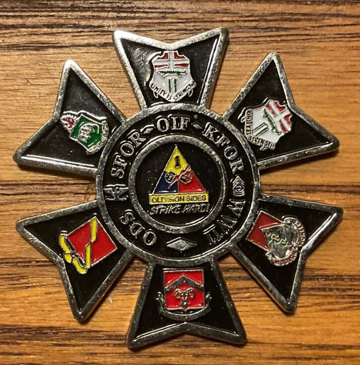 A US Army challenge coin. It is black and has 6 petals around a circular core. The circular core has the crest of the 2nd Brigade Combat Team/1st Armored Division surrounded by the name of the campaigns it has fought in. Each petal has the crest of each of the brigade's battalions: 1-6 Infantry, 2-6 Infantry, 1-35 AR, 4-27 Field Artillery, 40th Engineers, and the 47 Forward Support Battalion.