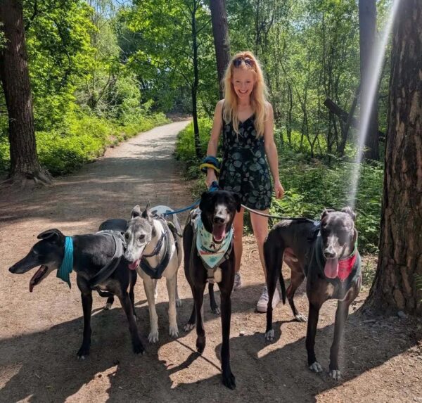 Hannah Spencer, MP for Gorton and Denton (Green Party), walking her four rescue greyhounds in a park on a sunny day.