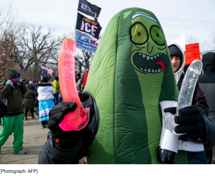 Person in a pickle costume holding two sex toys