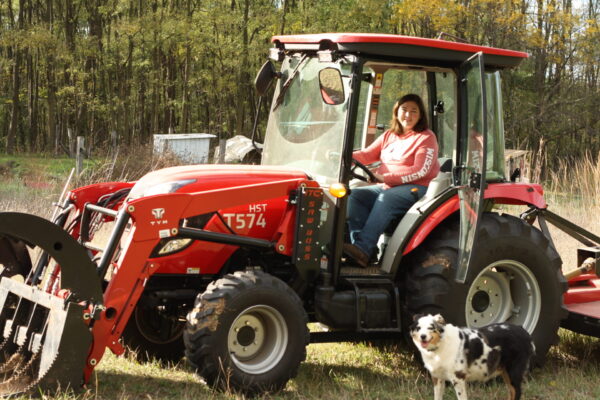 Amanda Bell on a red tractor with blue heeler mix next to it